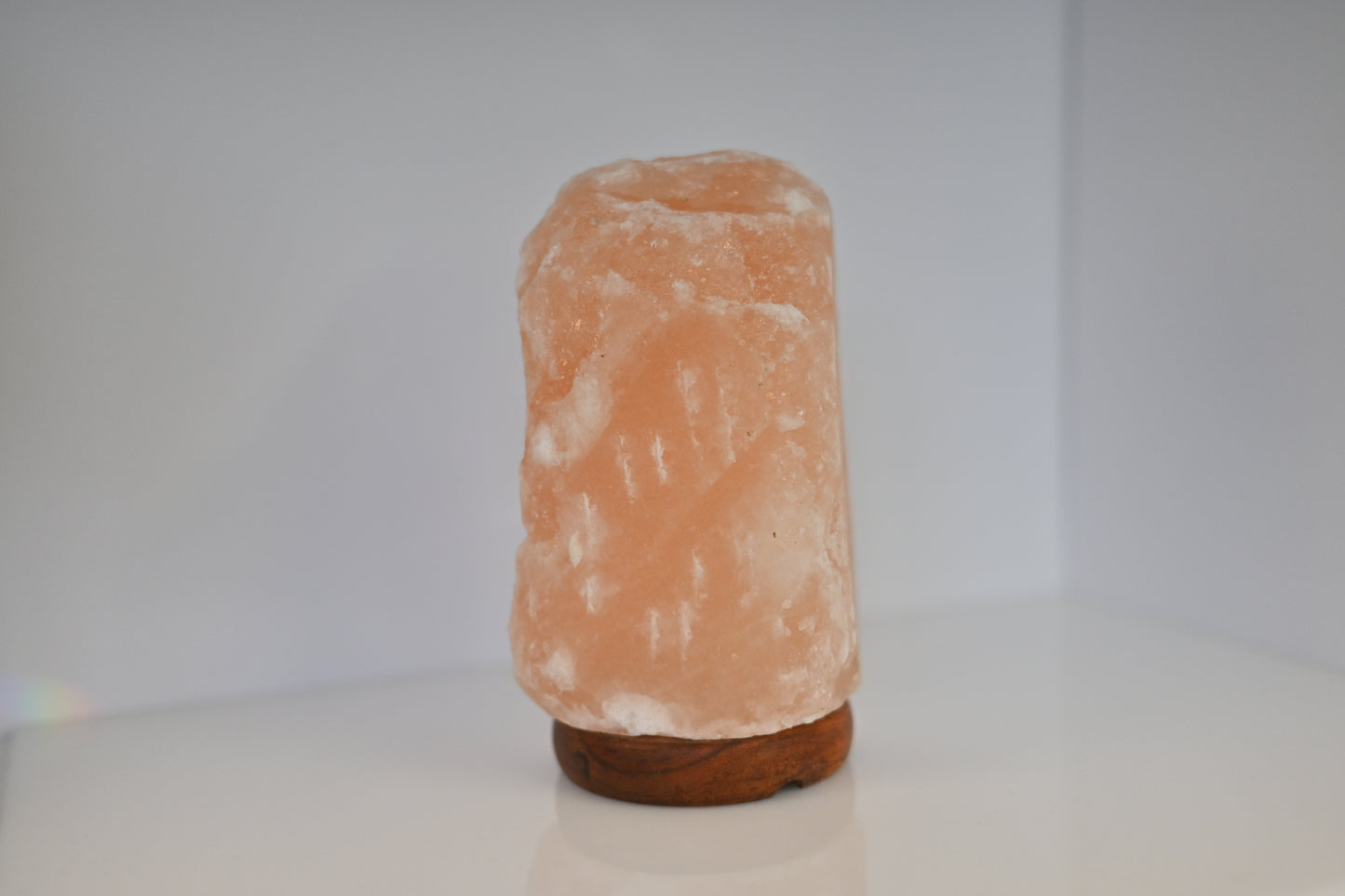 Lámpara de sal del Himalaya pequeña de 1-2 kg con base de madera encendida sobre una mesa.